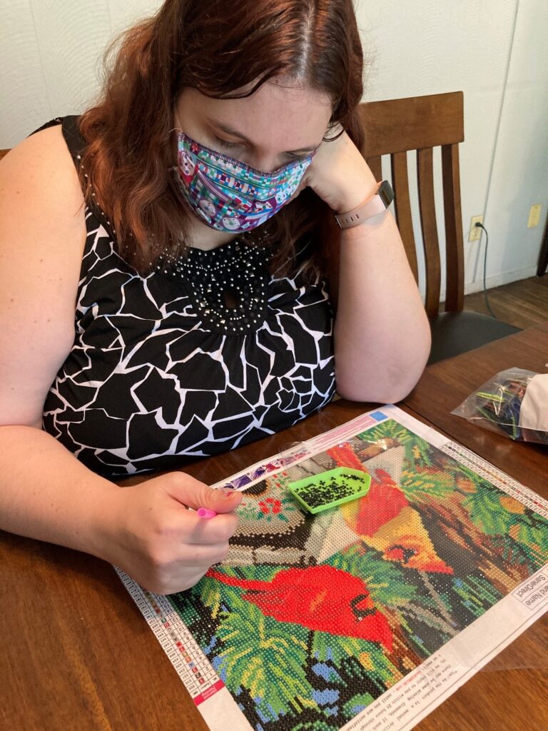 A picture of an individual with a mask doing an art project on the dining table.